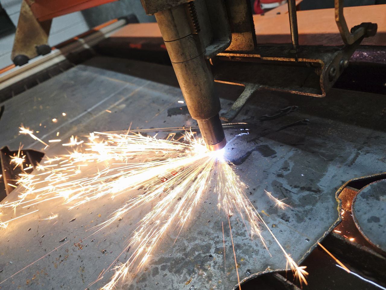 The CNC plasma torch cutting a sheet of steel as sparks fly