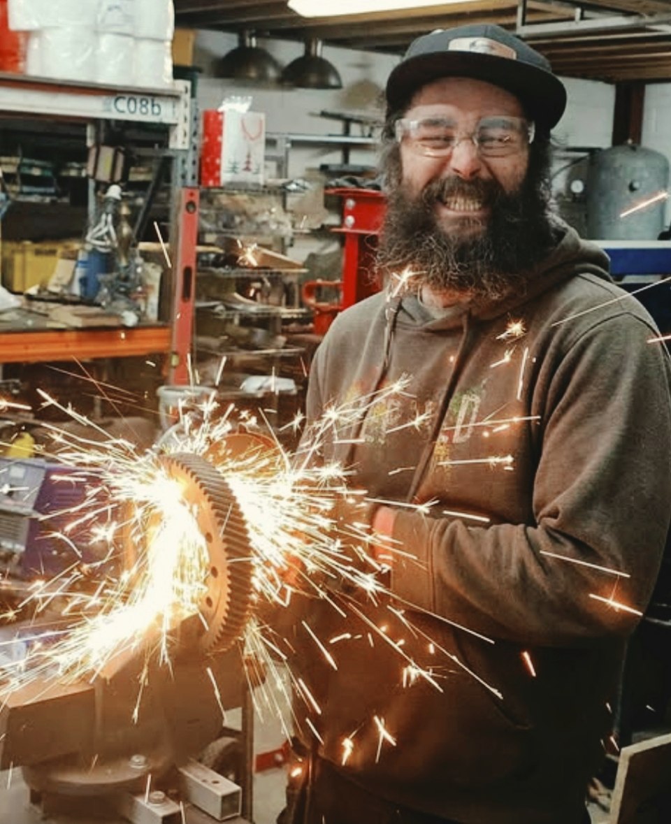 Jason smiling while grinding metal in the Rebuild Custom workshop as sparks fly