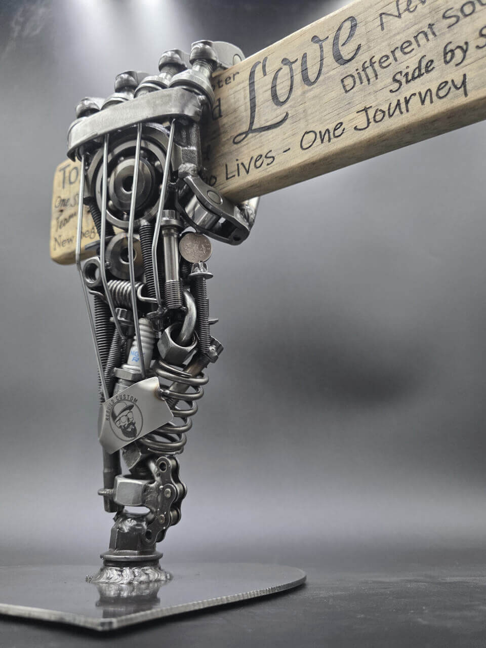 Scrap-metal hand sculpture holding a reclaimed pallet-board sign