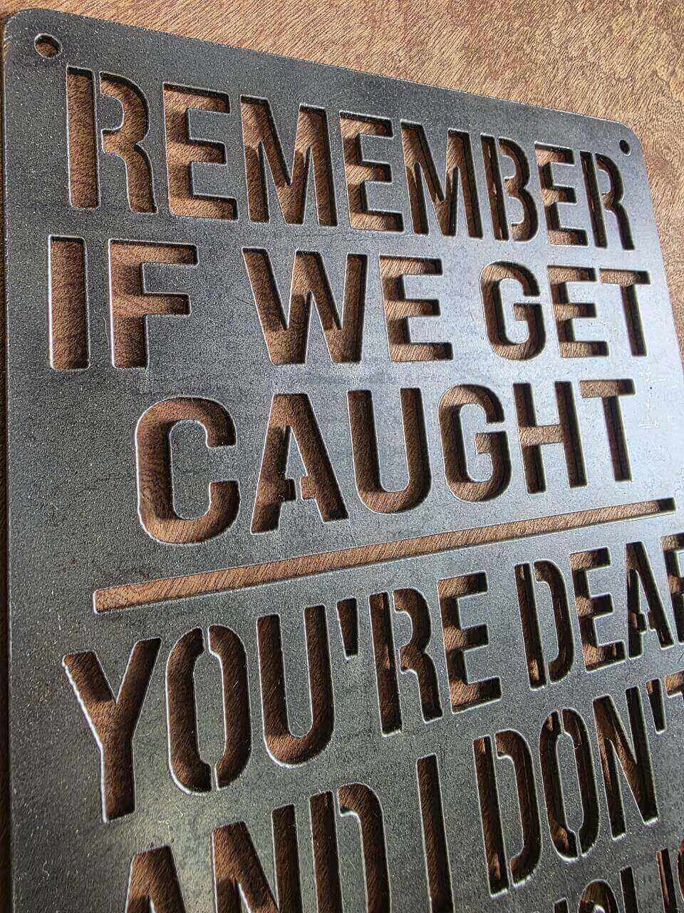 Angled view of Remember If We Get Caught metal sign