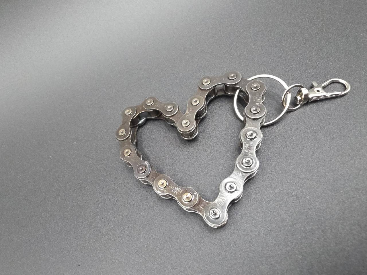 Handmade bicycle chain heart keyring on a dark background
