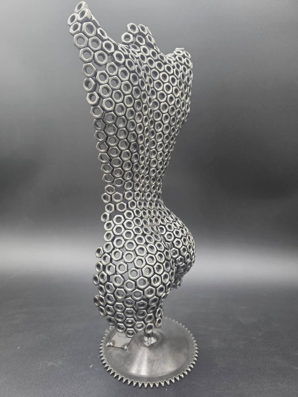 Angled rear view of the female torso sculpture made from stacked steel nuts