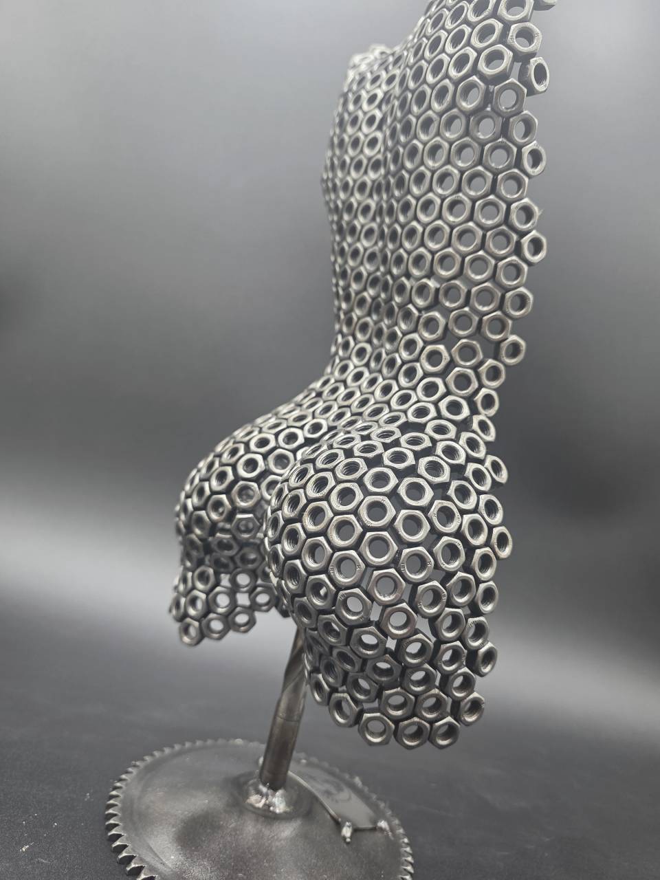 Profile view of the rear torso sculpture supported by a reclaimed drill bit
